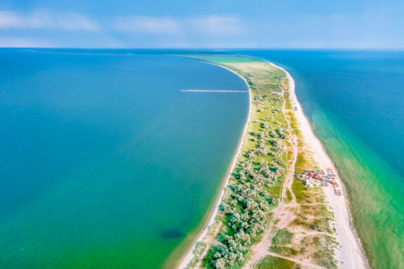 Aerial view of Kinburn Spit, a narrow strip of land with green vegetation between the blue waters of a sea and a lagoon.