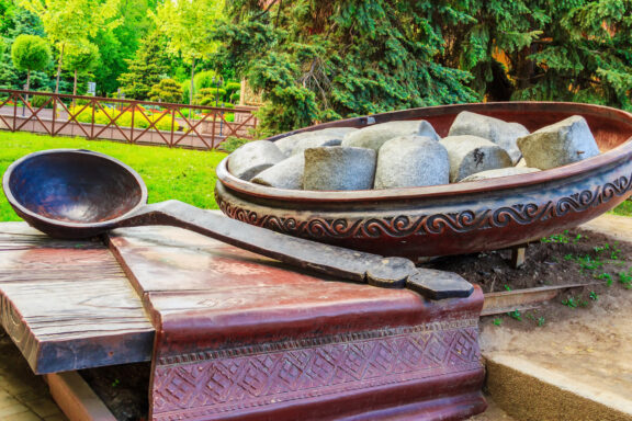 A traditional outdoor display in Poltava features a large carved wooden bowl with stone dumplings, table and spoon.