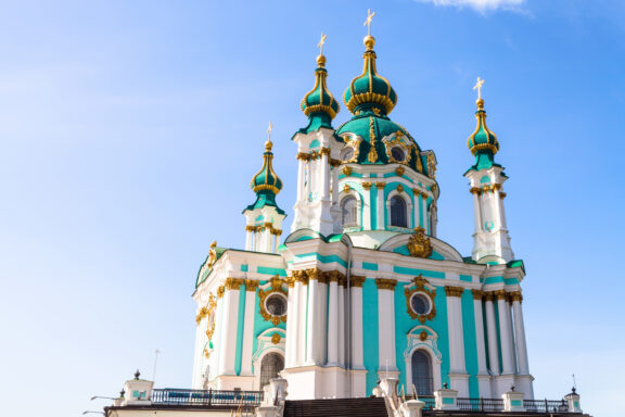 St. Andrew's Church in Kyiv with blue sky in the background, featuring green and gold domes and white Baroque architecture.