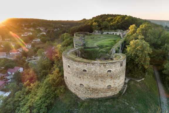 Aerial view of Terebovlia Castle ruins at sunset with surrounding greenery and a small town in the background, Terebovlia, Ukraine.