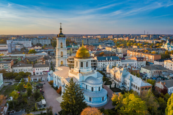 Aerial view of the white-walled, golden-domed Transfiguration Cathedral amidst trees and buildings in daylight.