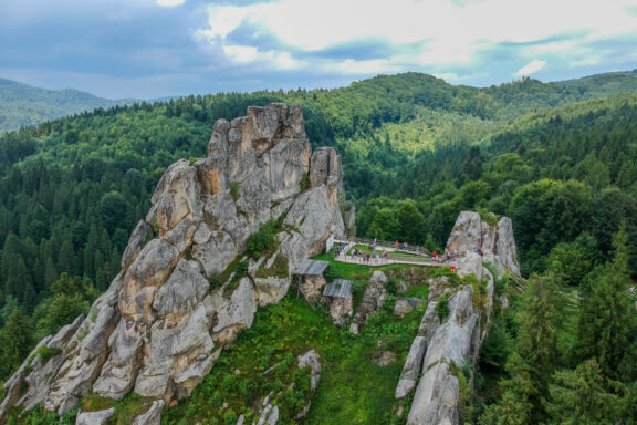 Aerial view of Tustan fortress ruins amidst forested hills, with rocky cliffs and greenery.