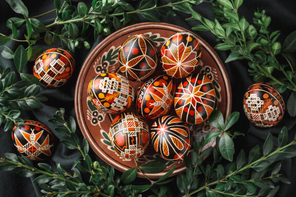 A collection of intricately decorated Ukrainian Easter eggs, known as pysanky, displayed on a plate surrounded by greenery.