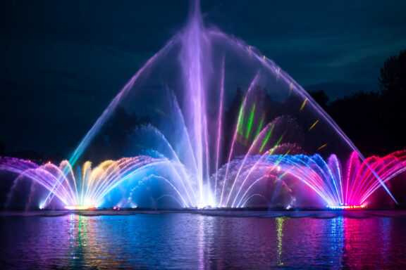 A colorful illuminated fountain at night in Vinnitsa, with water jets lit in hues of blue, pink, and purple against a dark sky.