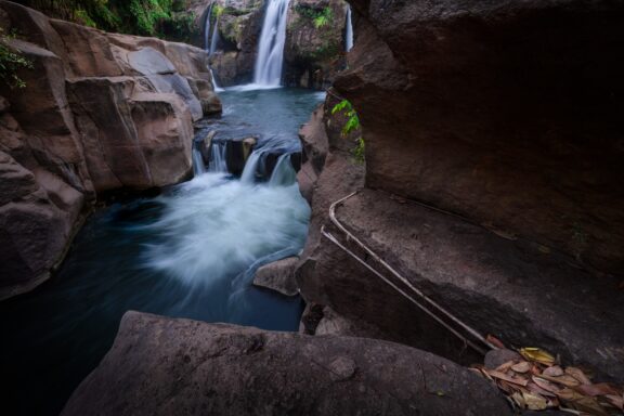 A serene waterfall cascading into a small pool surrounded by large rocks and a hint of greenery, located at Salto de Malacatiupan.