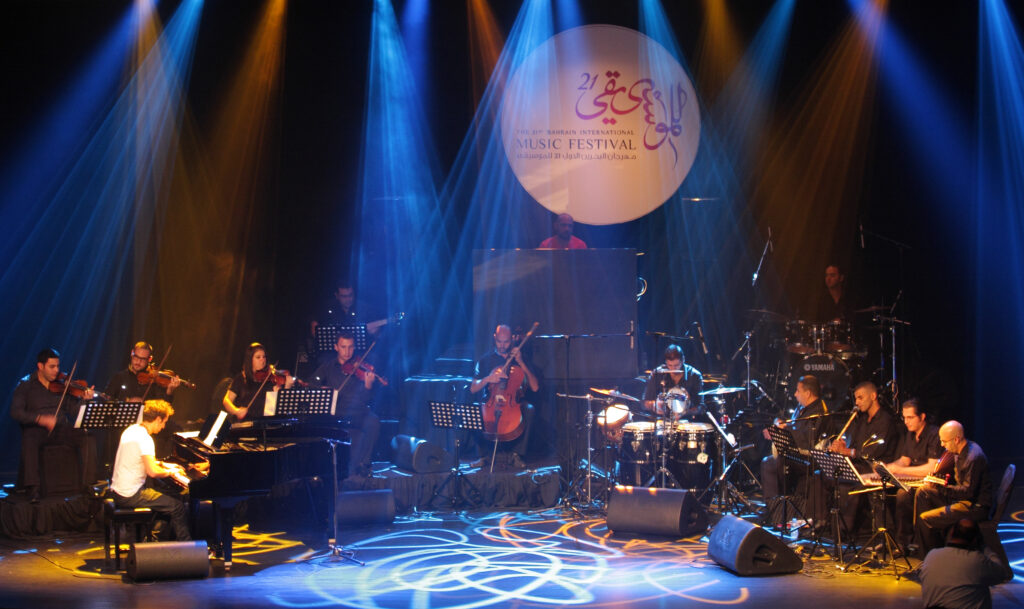 Musicians perform at the Bahrain International Music Festival, with a lit globe showing the festival's logo behind them.