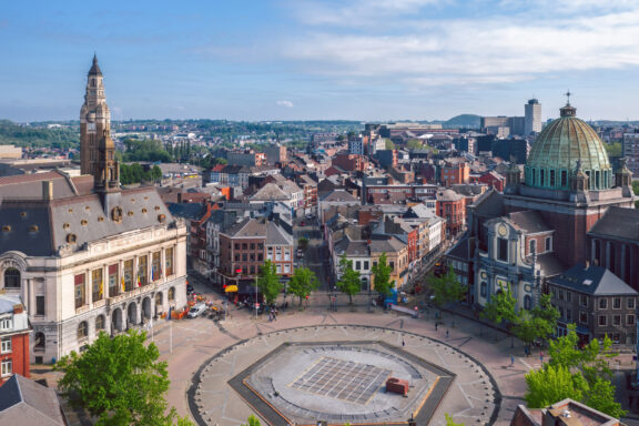 Aerial view of Charleroi, Belgium displays a mix of architectural styles, buildings, and a central town square under a cloudy sky.