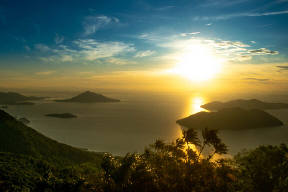 Sunset view over a lake with silhouettes of volcanic islands and a foreground of foliage, likely taken from Conchagua Volcano in El Salvador.