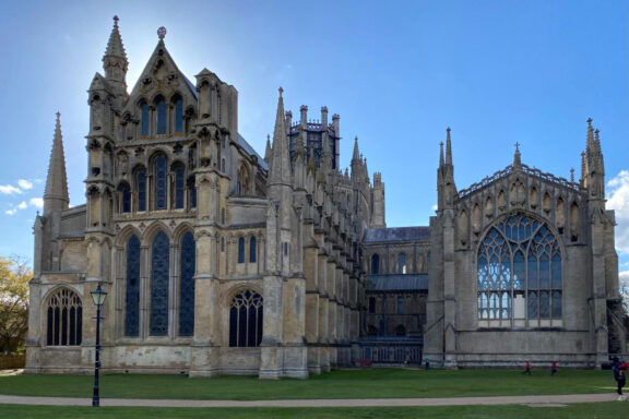 Ely Cathedral, a large and ornate Gothic cathedral with intricate architectural details, under a clear blue sky.