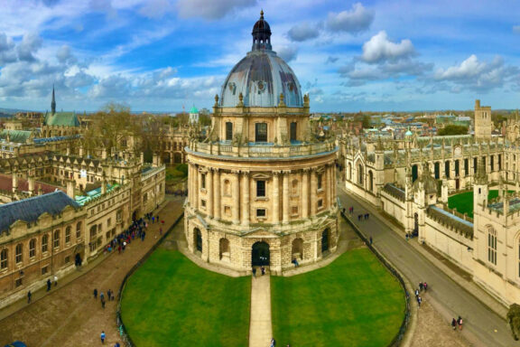 Aerial view of Oxford University's neoclassical Radcliffe Camera, surrounded by green lawns and historic buildings.