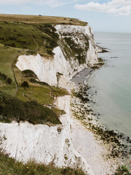 A picturesque view of the UK's White Cliffs of Dover, showcasing white chalk cliffs, greenery, sea, and clear sky.