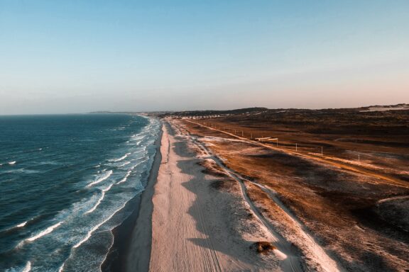 Aerial view of a beach in Ceará, Brazil, showing the coastline with waves, sandy shore, and adjacent land during twilight.