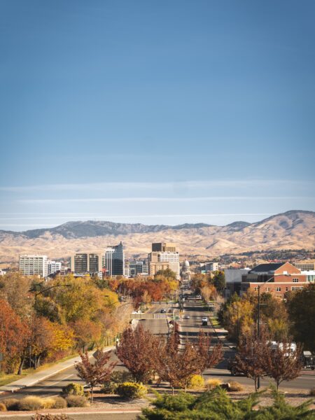 Boise, Idaho's skyline is showcased against rolling hills and a blue sky, with autumn colors in the trees.