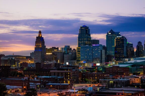 A twilight view of Kansas City skyline with illuminated buildings under a gradient sky.