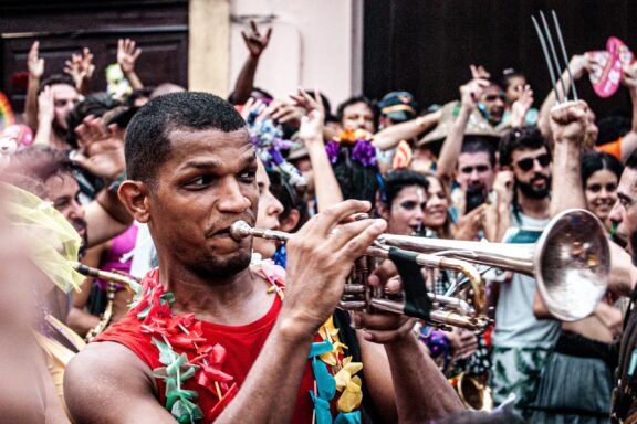 A man playing the trumpet at Carnaval, surrounded by a crowd of people celebrating.