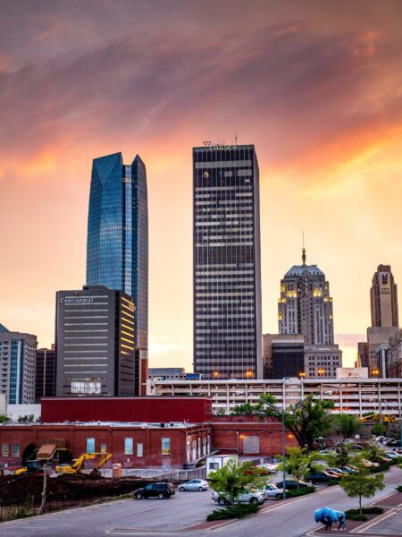 A sunset view of the Oklahoma City skyline with prominent buildings under an orange sky.