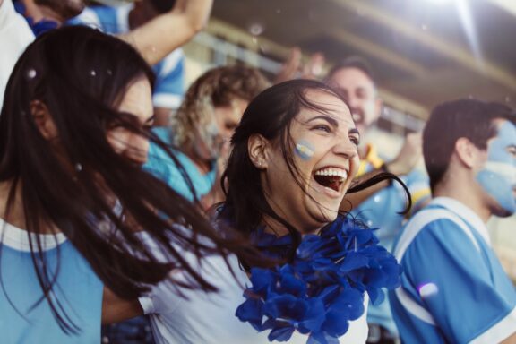 A group of jubilant soccer fans wearing blue and white, the colors associated with Argentina, cheering at a match.