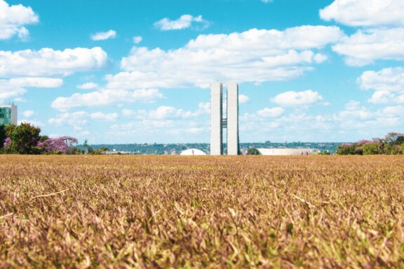 A photo depicts the Brasília National Congress towers in the distance, set against dry grass and a clear sky.