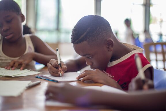 A group of children in Equatorial Guinea engaged in writing activities at a table.