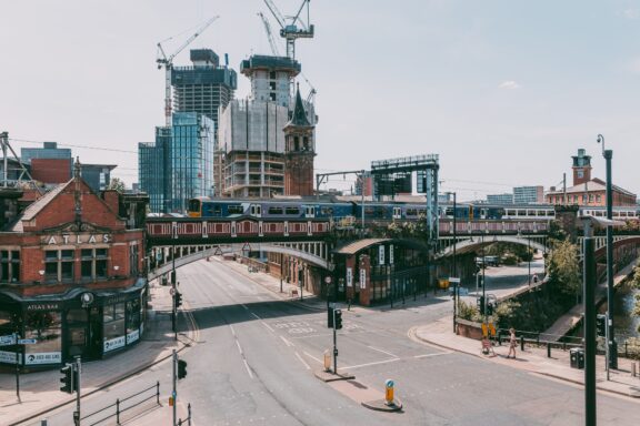 A cityscape with construction cranes over buildings, an overpass, and empty streets.