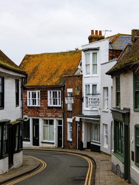 A quaint, possibly historic town with a narrow, curving street lined with traditional buildings, some with visible signs.