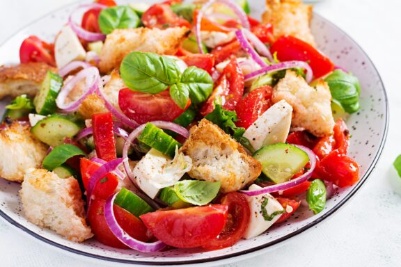 A vibrant panzanella salad featuring ripe tomatoes, cucumbers, red onions, basil, bread chunks, seasoned with olive oil and herbs.