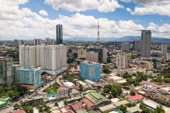 Aerial view of Quezon City with high-rise buildings, scattered clouds, and a cityscape extending into the horizon.