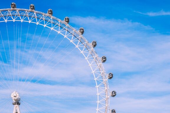 A section of a large Ferris wheel with enclosed capsules against a blue sky with wispy clouds.