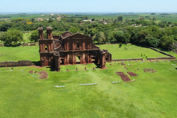 Aerial view of the ruins of São Miguel das Missões in a green landscape, under a clear sky.