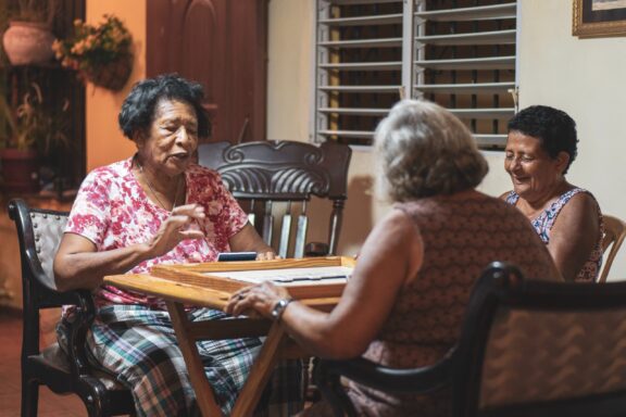 Three elderly individuals are conversing and enjoying each other's company in a homely setting in Santo Domingo.