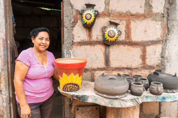 A woman in a pink striped shirt smiling next to a table with pottery and a colorful painted bucket, in Nicaragua.