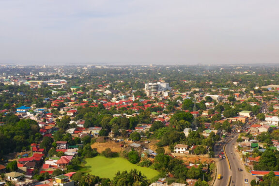 Aerial view of Zamboanga City with buildings, roads, and greenery under a hazy sky.