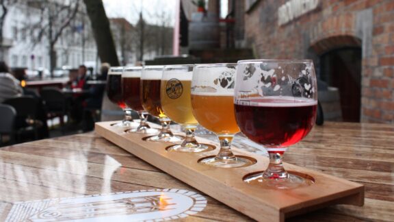 Belgian beers in various glasses on a wooden paddle, displayed outdoors, possibly in Belgium.