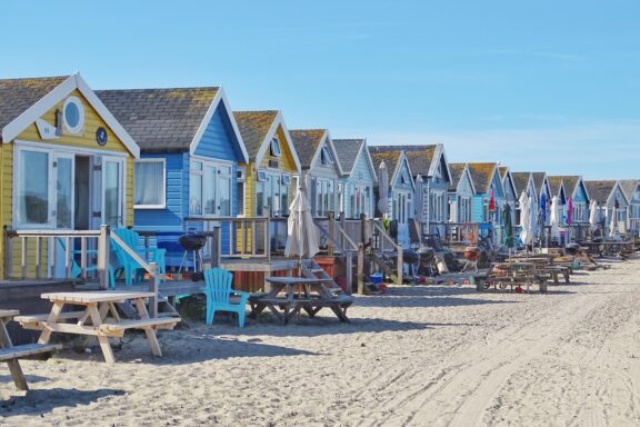 A row of colorful beach huts on Bournemouth Beach with sand in the foreground and a clear blue sky above.