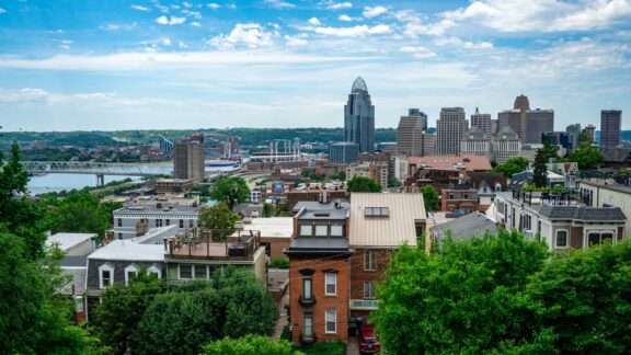 A panoramic view of Cincinnati, Ohio features the city skyline, Ohio River, and residential buildings.