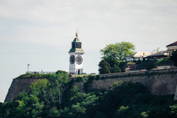 A clock tower atop a grassy hill with a clear sky in the background, located in Novi Sad.