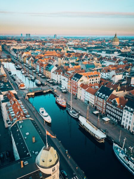 Aerial view of Copenhagen, Denmark, showcasing colorful buildings along a canal with boats, streets, and a clear sky during twilight.