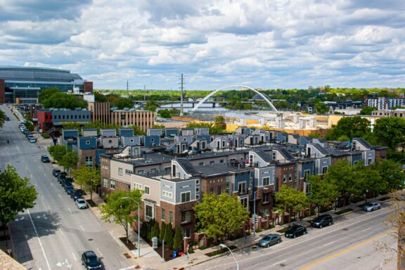 Daytime view of a Des Moines, Iowa street with multi-story buildings, a bridge, and larger structures under a partly cloudy sky.