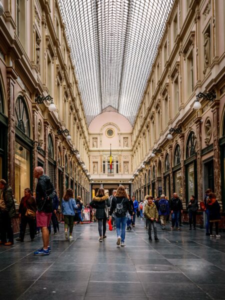 An image of people walking inside the Galeries Royales Saint-Hubert in Brussels, featuring an arched glass ceiling and elegant shopfronts.