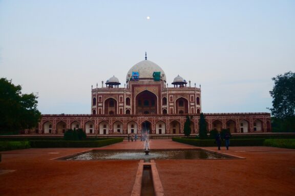 A photo of Humayun's Tomb in Delhi, India, with a symmetrical view of the mausoleum across a water channel, during twilight or early evening.