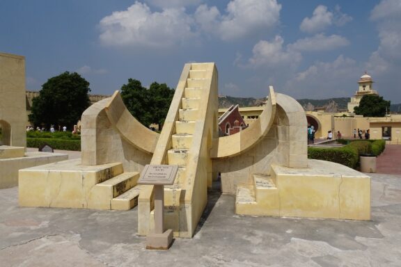 The image shows the Jantar Mantar astronomical observatory in Jaipur, India, featuring a large sundial structure under a clear sky.