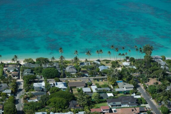 Aerial view of a coastal residential area in Kailua, Hawaii, with clear turquoise waters and scattered palm trees.