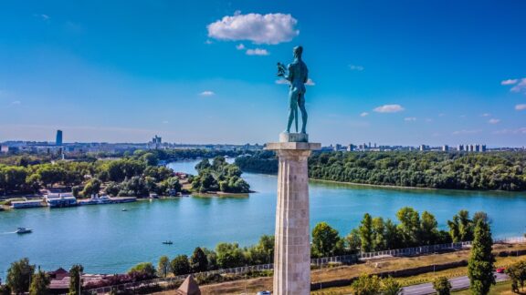 Aerial shot of Pobednik monument in Belgrade's Kalemegdan Park, overlooking the Sava and Danube rivers under clear skies.