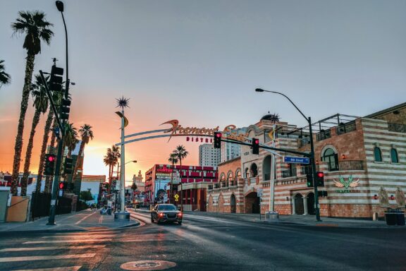 A street view at dusk in Las Vegas, Nevada, with palm trees lining the road, a colorful sky, and illuminated signs.