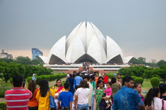 People stand before the Lotus Temple in New Delhi, India, a unique flower-shaped marble structure on an overcast day.