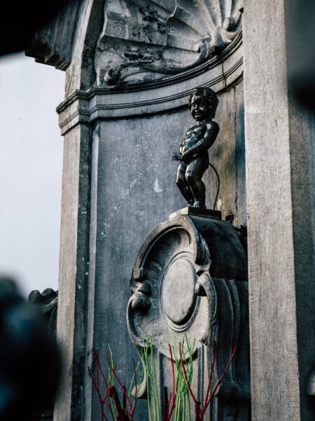 A statue of the Manneken Pis, a famous landmark in Brussels, depicted as a small bronze boy urinating into a fountain's basin.