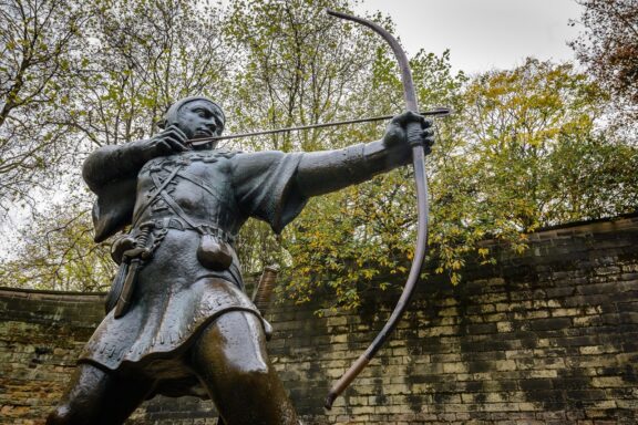 A statue of Robin Hood with a bow and arrow in Nottingham, surrounded by trees with autumn leaves.