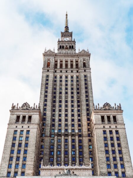 An image of the Palace of Culture and Science in Warsaw, Poland, showing the towering structure against a cloudy sky.