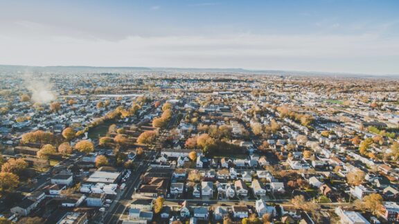 Aerial view of a suburban area in Paramus, New Jersey, with rows of houses and autumn-colored trees, under a partly cloudy sky.