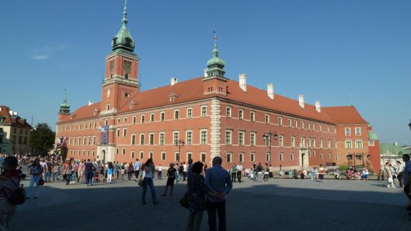 A photo of the Royal Castle in Warsaw, Poland, with people walking in the foreground during the daytime.